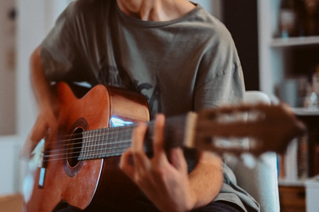Musician playing a wooden acoustic guitar in an indoor room.